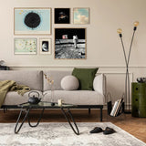 A styled living room interior featuring a light gray sofa with green and beige throw pillows, a glass-top coffee table, a patterned rug, wall art, and a black sideboard against a beige wall.