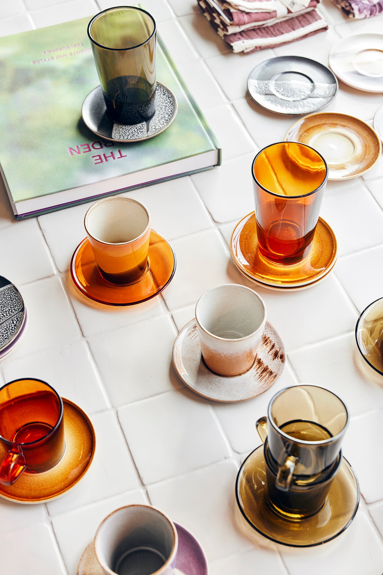 Collection of colorful glass cups and saucers on a white tiled surface with a book in the background.