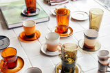 Collection of colorful coffee cups and saucers on a tiled surface.