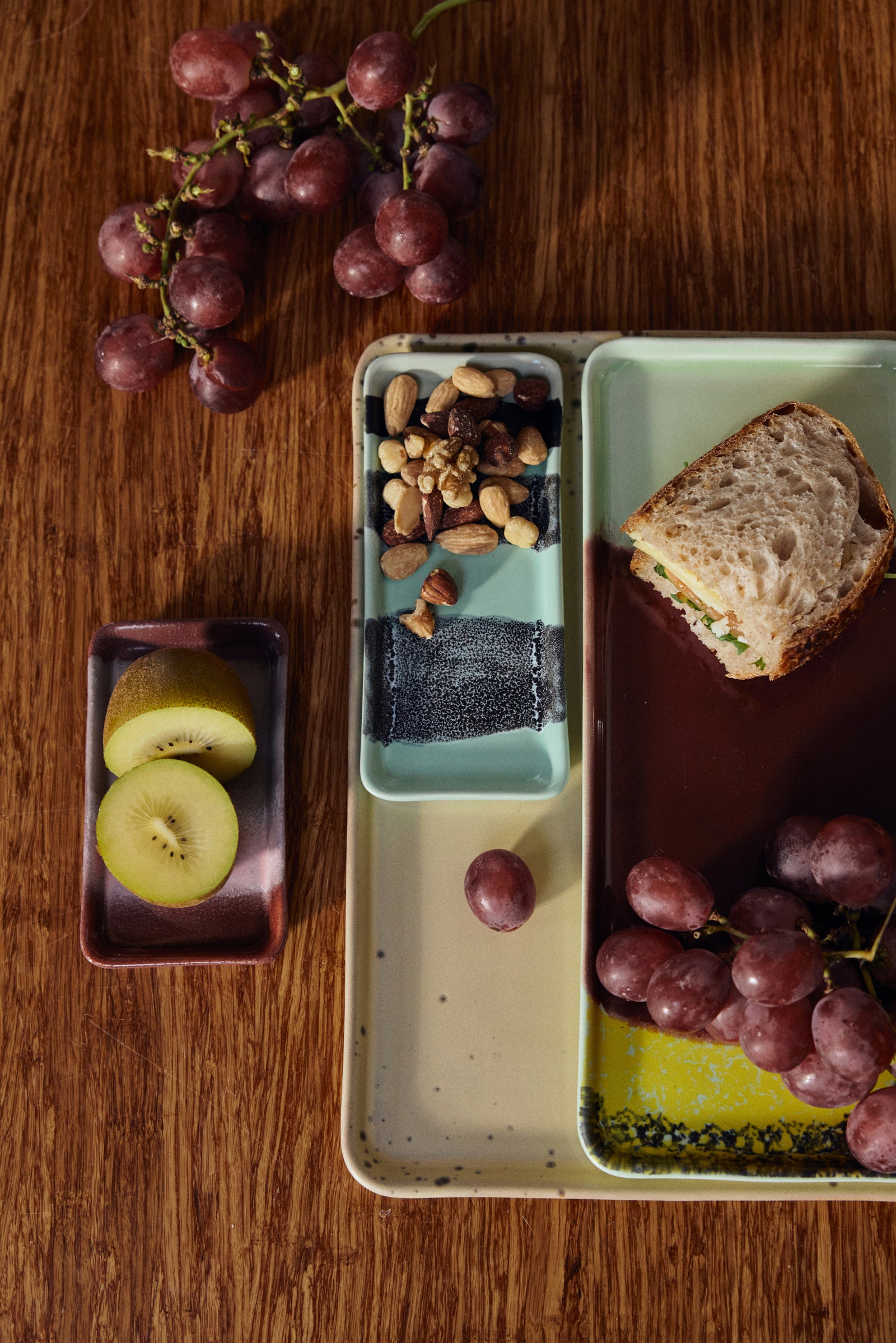 Snack platter with grapes, apples, nuts, and bread on a wooden surface