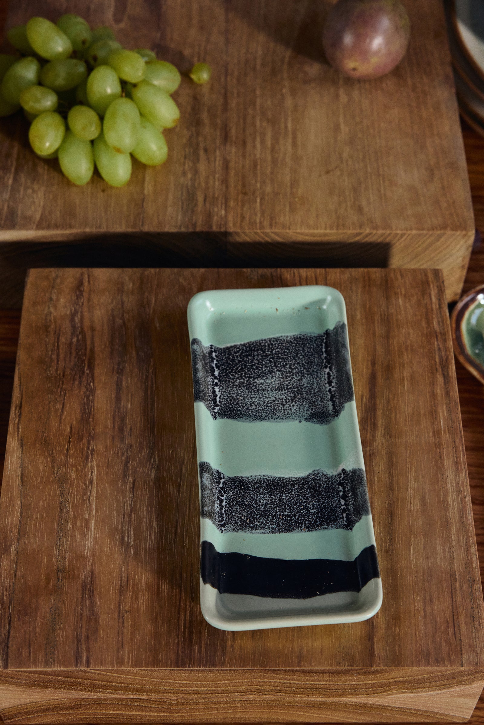 Rectangular ceramic dish with black stripes on a wooden surface with grapes in the background