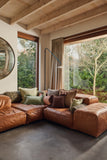 Modern living room with brown leather sectional sofa and large windows.