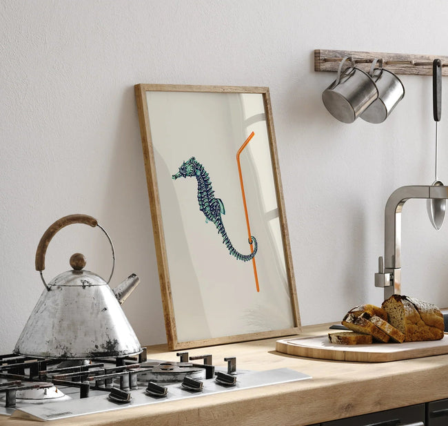 Kitchen counter with a kettle, framed picture of a seahorse, and bread on a cutting board.