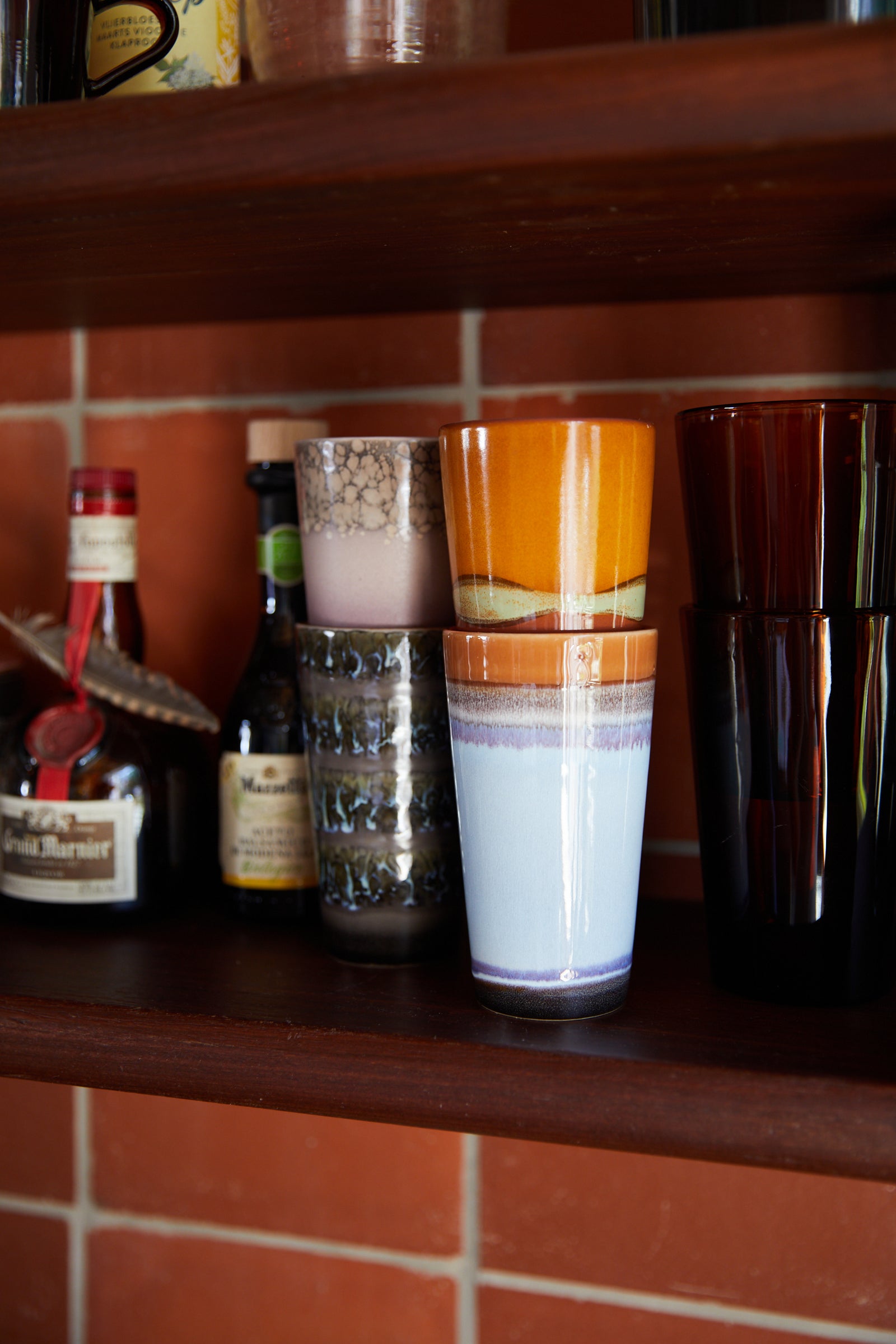 Collection of vintage cups and bottles on a wooden shelf with a tiled wall background