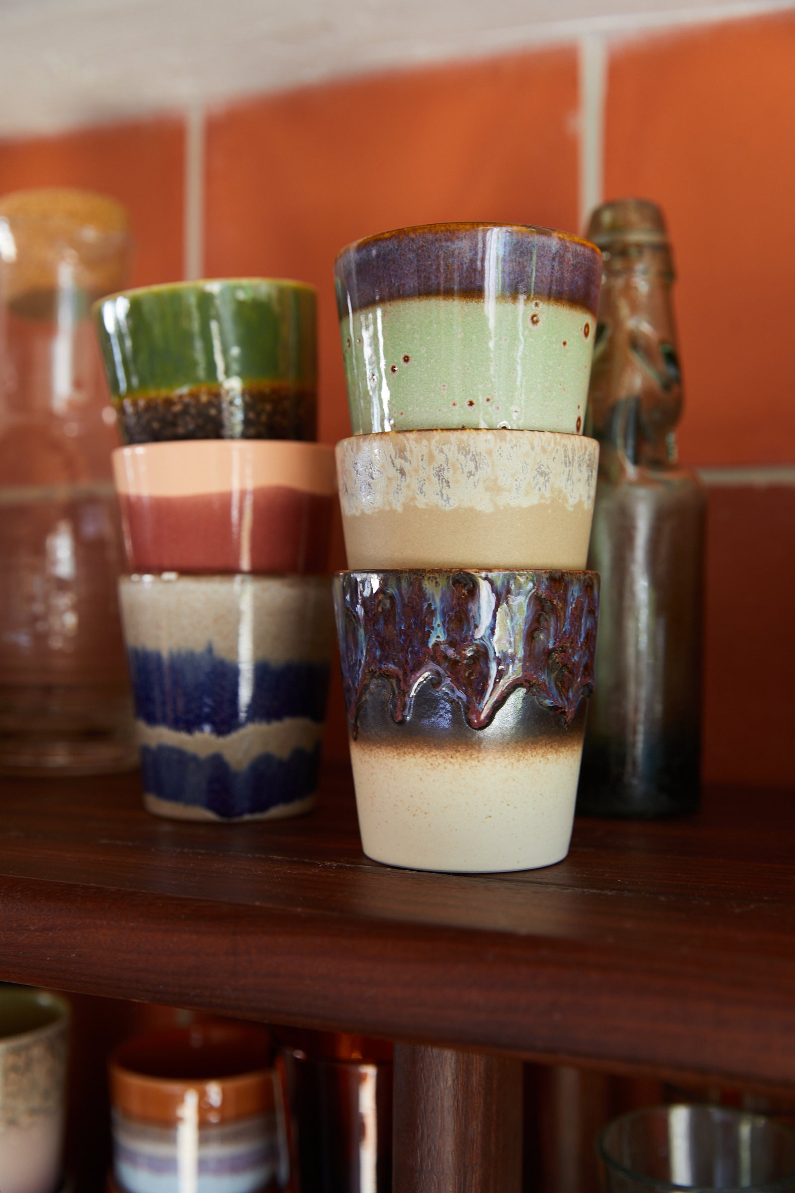 Stack of ceramic cups with multicolored glaze on a wooden shelf.