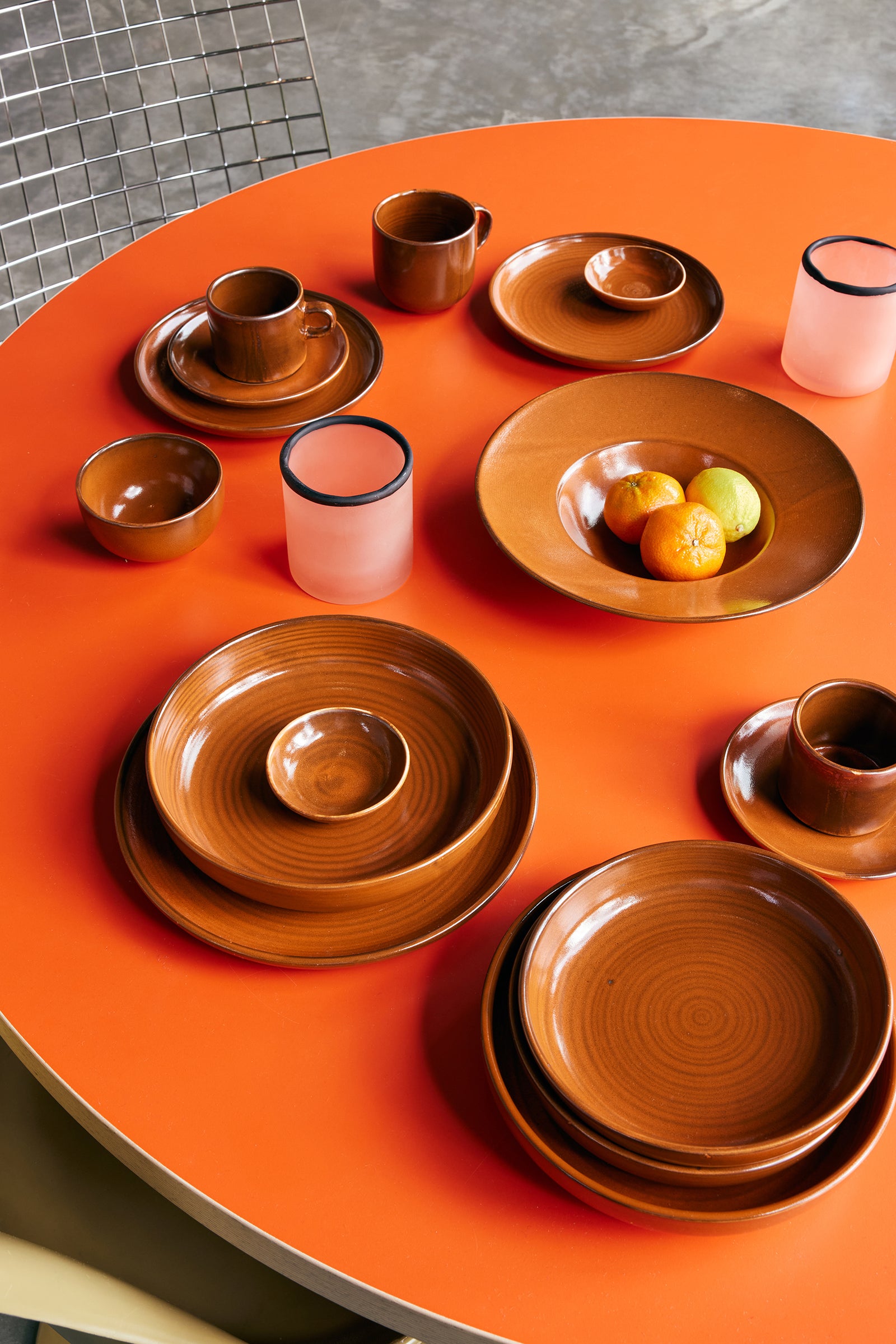 Set of brown ceramic dishes on an orange table with a tiled floor background