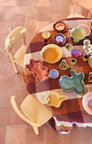 Round wooden table with colorful ceramic plates and cookie cutters on a tiled floor.