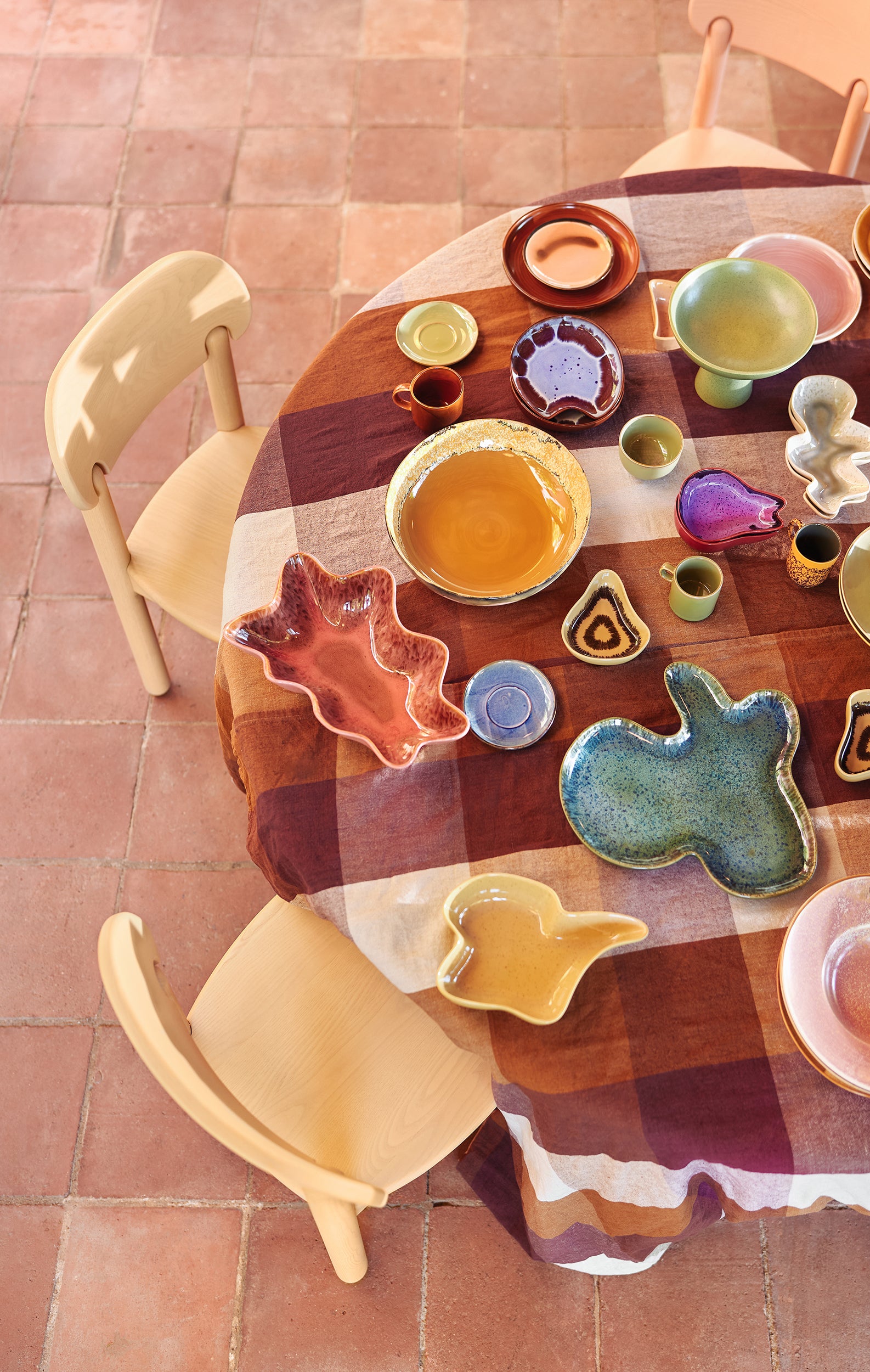 Round wooden table with colorful ceramic plates and cookie cutters on a tiled floor.