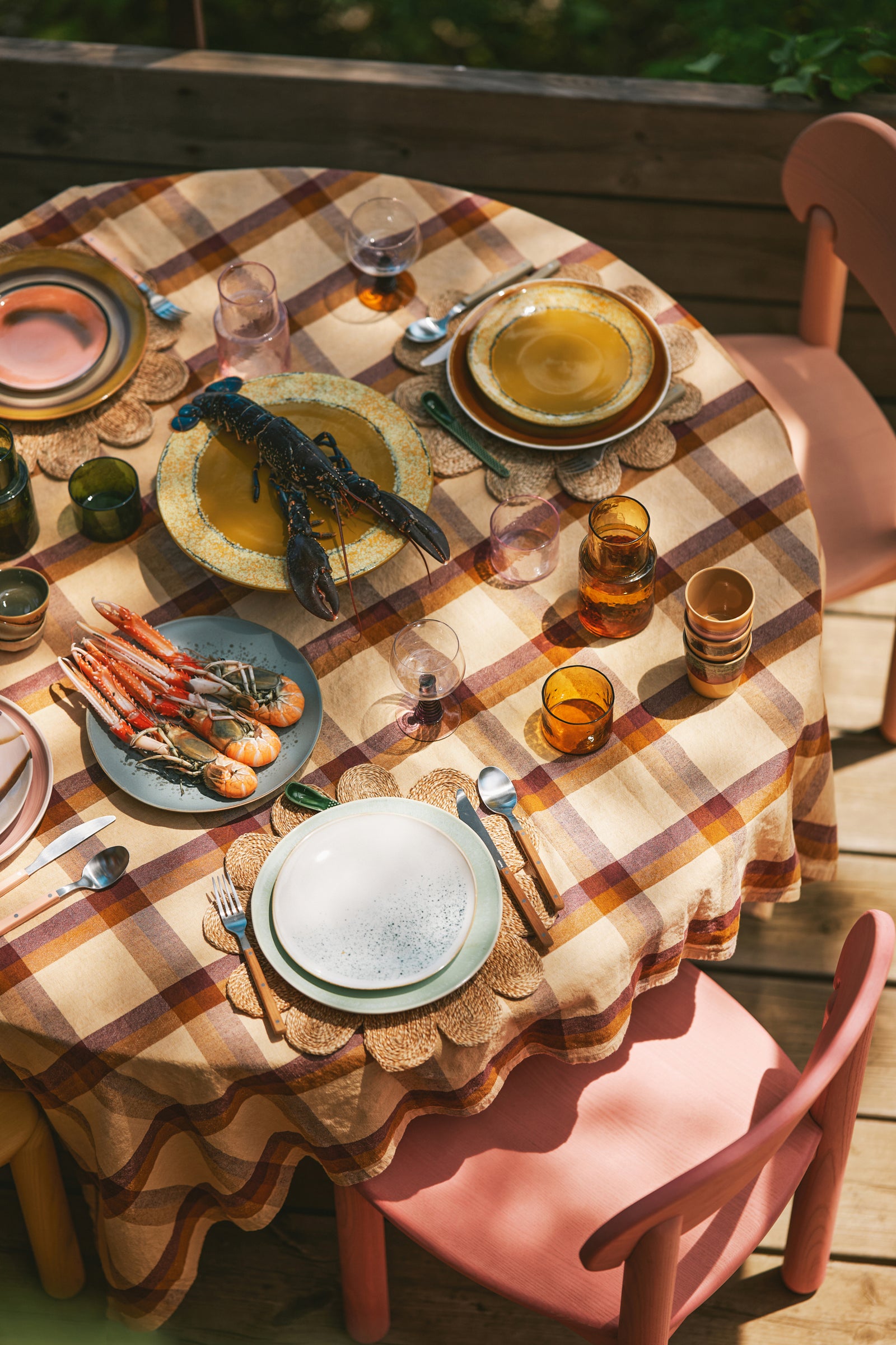 Dining table set with plates, glasses, and cutlery on a checkered tablecloth outdoors.