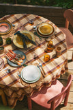 Dining table set with plates, glasses, and cutlery on a checkered tablecloth outdoors.