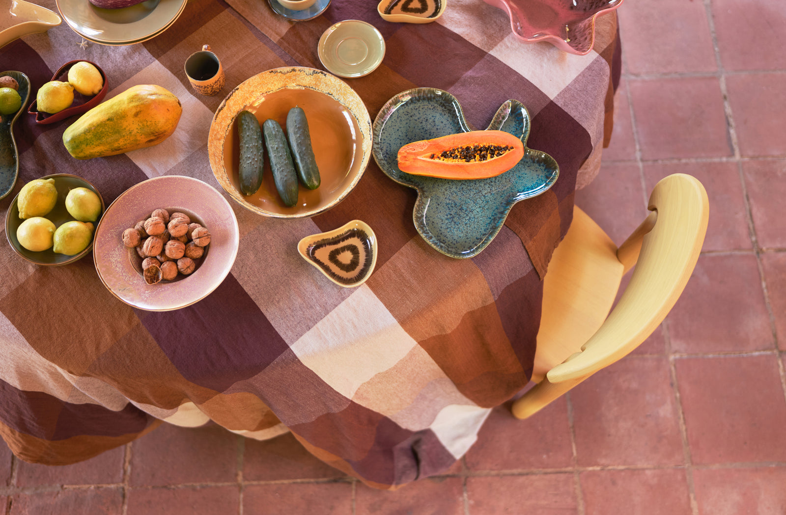 Table setting with ceramic plates and bowls containing fruits and vegetables on a checkered tablecloth.