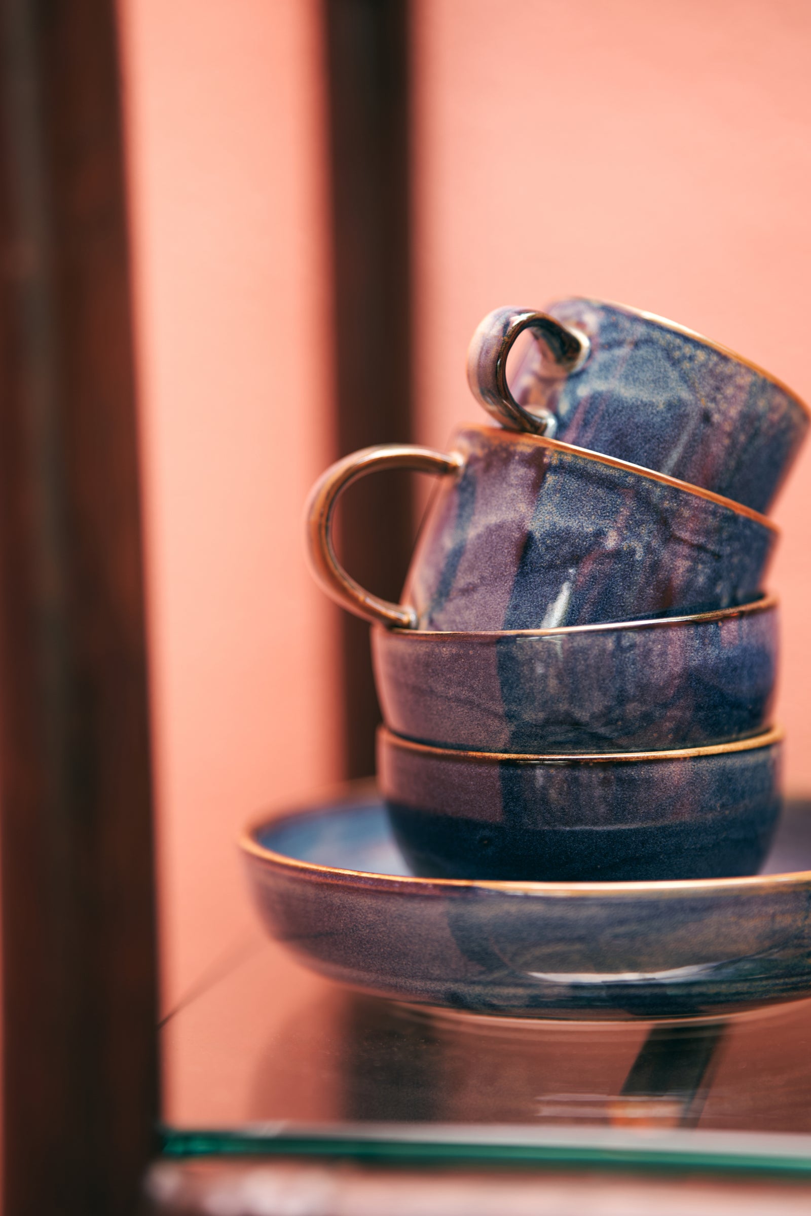 Stack of blue ceramic teacups with gold accents on a reflective surface.