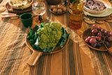Table setting with a head of cauliflower on a wooden board, grapes, and other dishes.