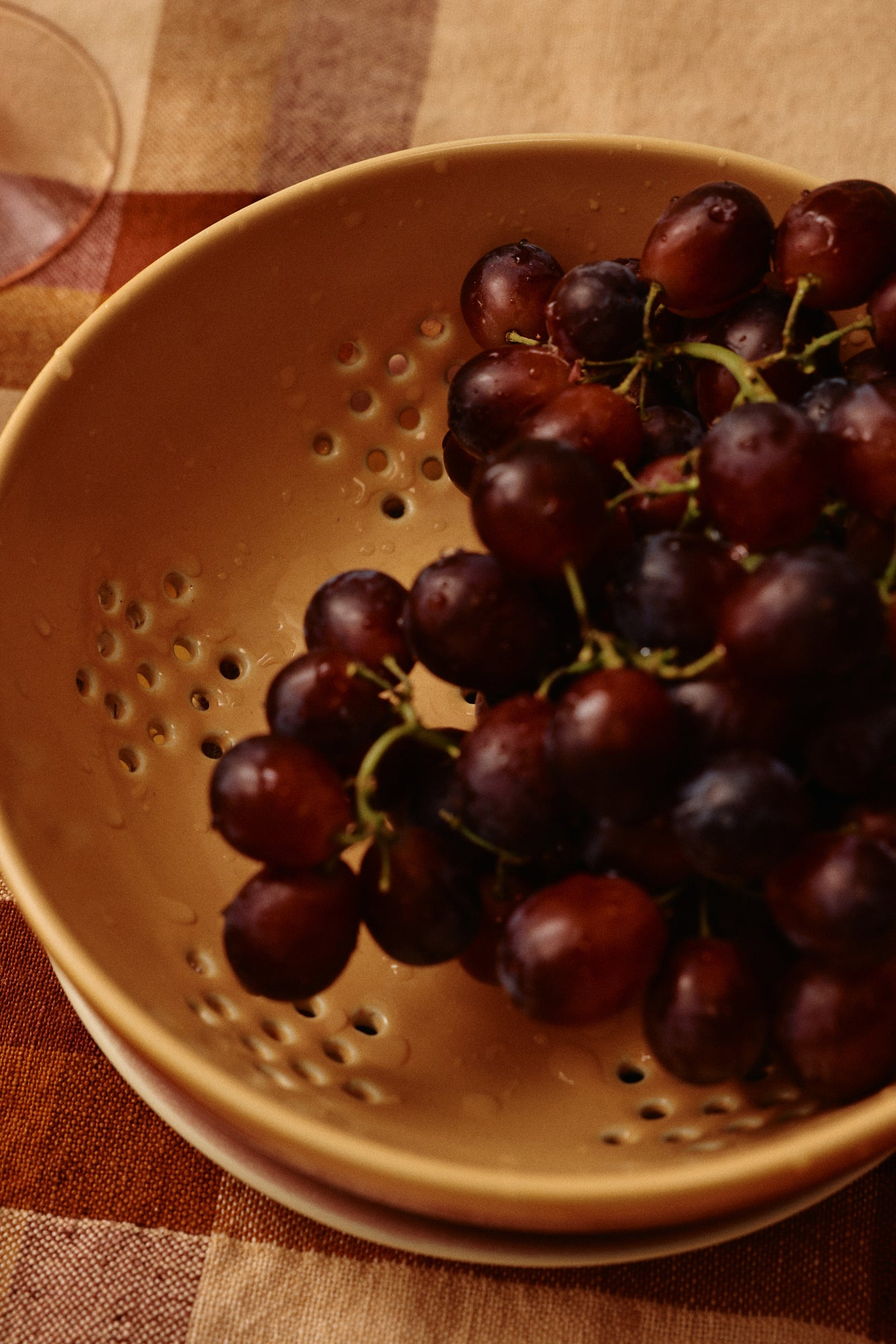 Red grapes in a yellow colander on a checkered tablecloth
