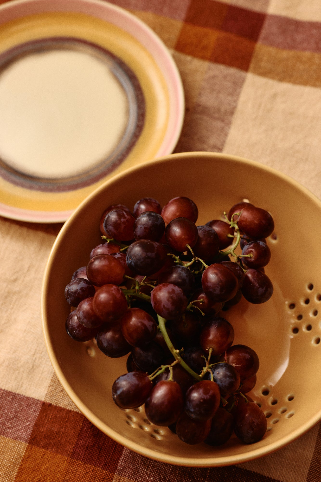 Bunch of grapes in a yellow colander on a checkered tablecloth