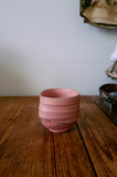 Pink ceramic cup on a wooden surface with a neutral background