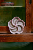 Ceramic flower-shaped dish on a wooden shelf with a green wall in the background