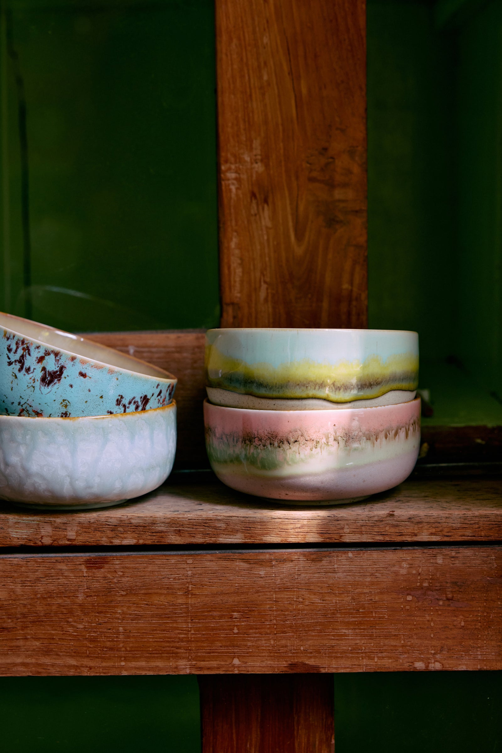Three ceramic bowls with colorful glazes on a wooden surface against a green background