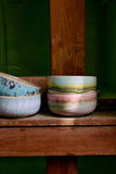 Three ceramic bowls with colorful glazes on a wooden surface against a green background