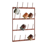 A rust-colored metal mug rack with five horizontal bars and multiple vertical hooks, shown against a plain white background with several ceramic mugs displayed on it.