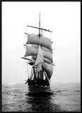 Black and white photograph of a tall-sailed historical sailing ship with multiple masts and billowing sails, sailing on open water under a cloudy sky.
