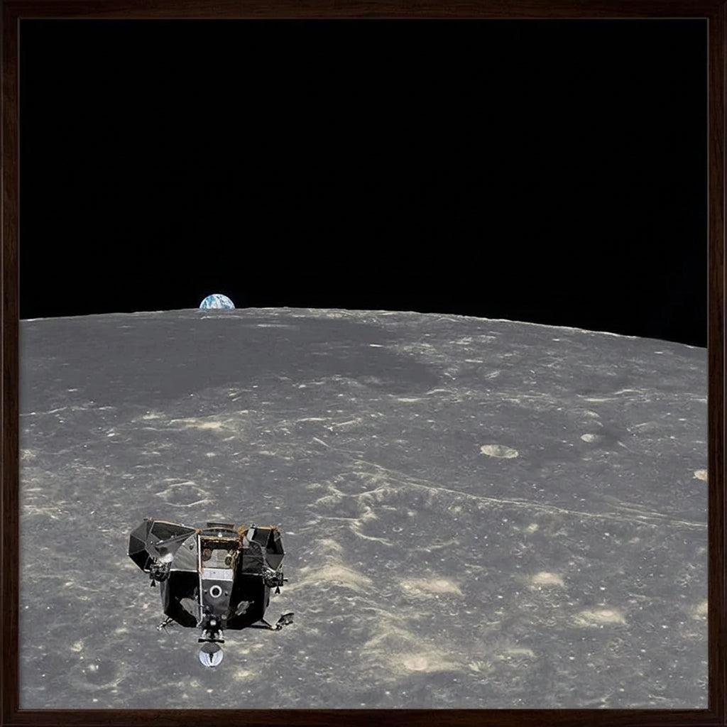 A framed space-themed artwork showing a lunar lander on the surface of the Moon with Earth visible in the black outer space background, enclosed in a light wood frame.