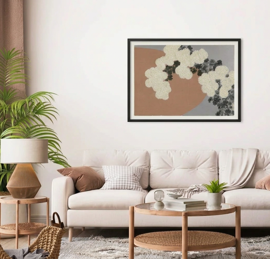 A framed abstract wall art print hangs above a light beige sofa in a styled living room. The artwork features a large warm tan shape, a gray section, and white and dark gray floral or cloud-like forms.