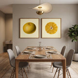 A styled bathroom scene with two framed botanical-style fruit prints hanging above a yellow clawfoot bathtub. The left print shows a whole yellow citrus fruit, and the right print shows a sliced orange-yellow citrus cross-section.