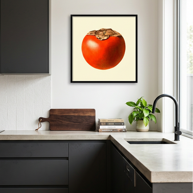 A framed art print of a red persimmon on a cream background, displayed on a white wall in a modern kitchen with dark gray cabinets and light countertops.