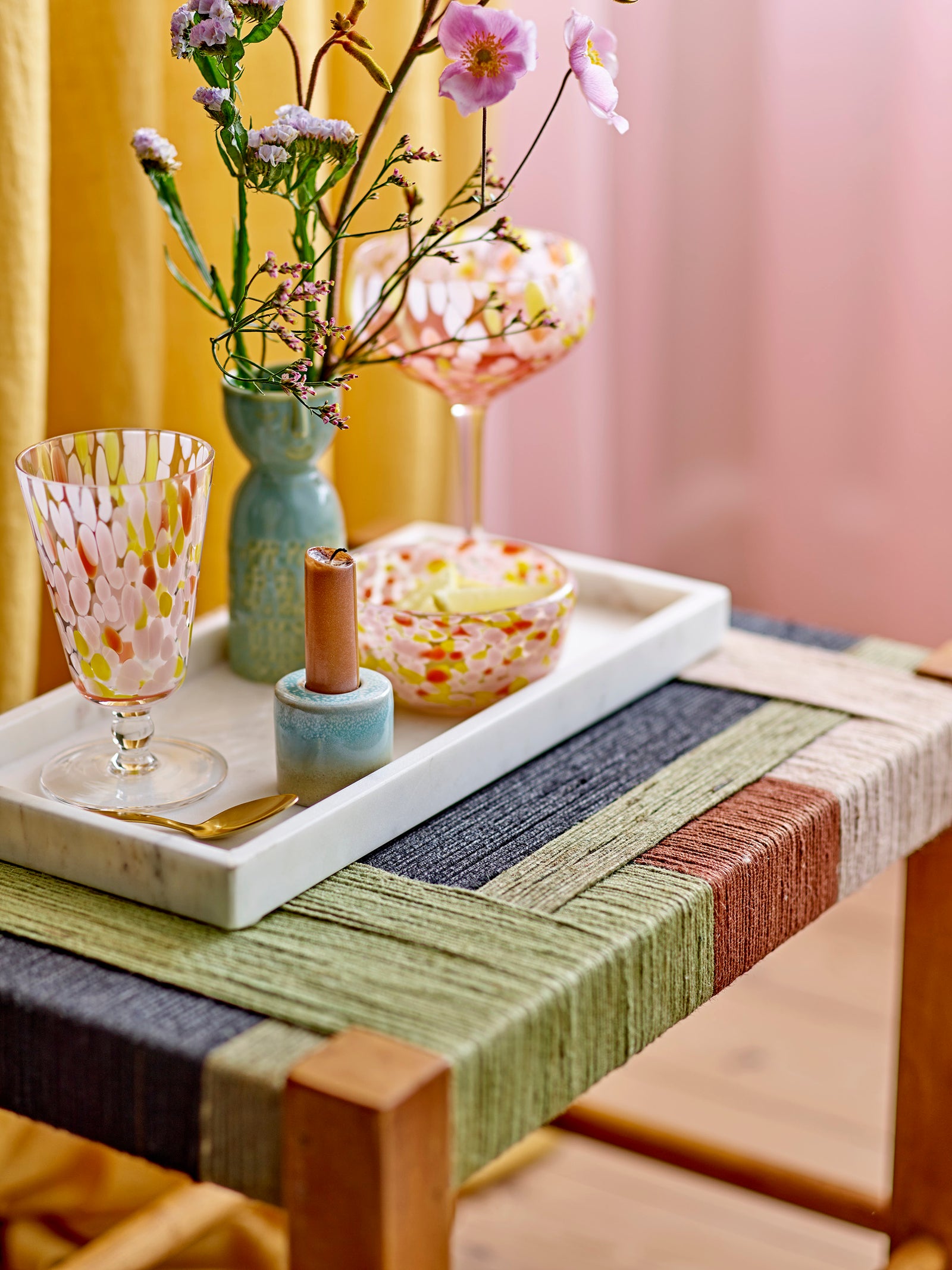 Decorative tray with a woven placemat, glasses, and flowers on a table.