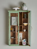 Wooden cabinet with glass doors displaying various items against a plain wall.