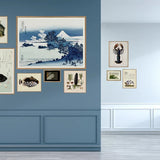 A gallery wall display featuring multiple framed art prints, including a large Japanese-style landscape print, a blue-and-white Mount Fuji scene, and smaller botanical and architectural illustrations, mounted on a blue wall in a modern interior.