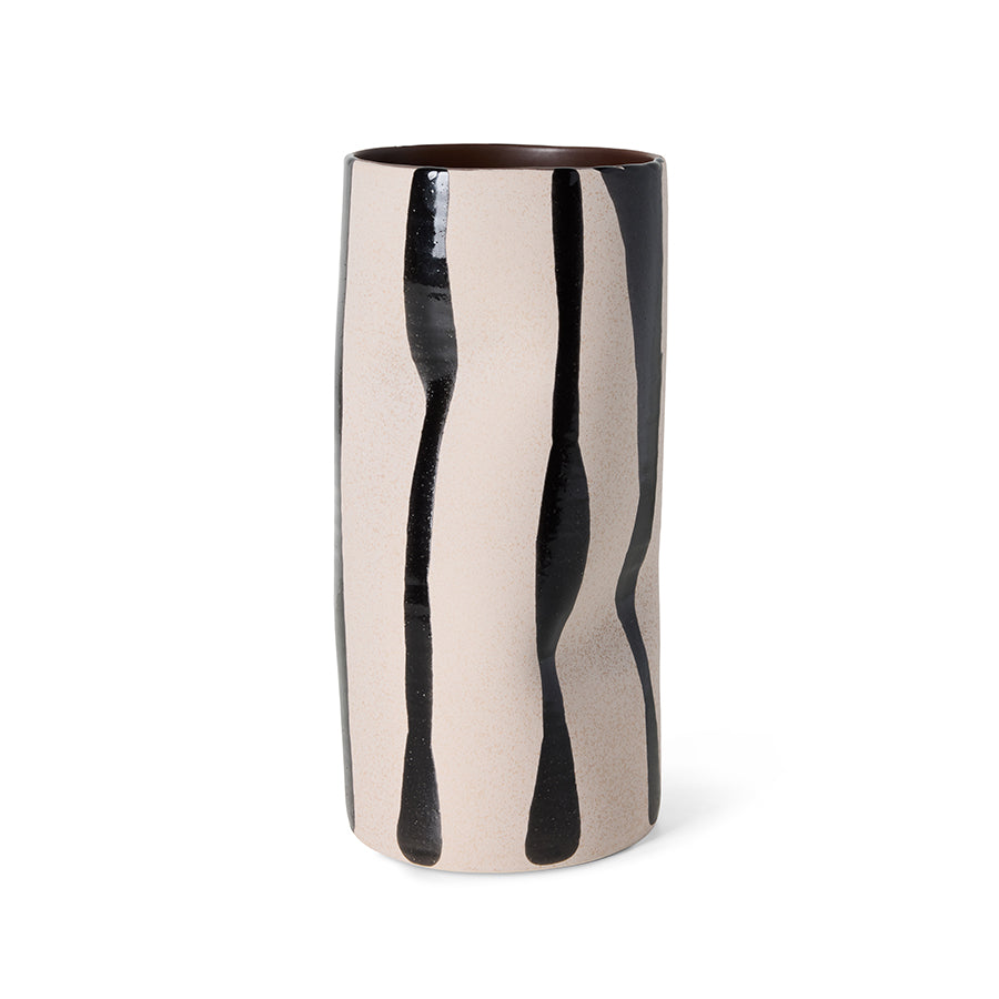 A tall cylindrical ceramic vase with a glossy finish, featuring a beige and black abstract dripping pattern, set against a plain white background.