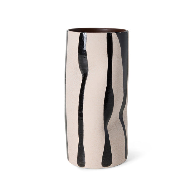 A tall cylindrical ceramic vase with a glossy finish, featuring a beige and black abstract dripping pattern, set against a plain white background.