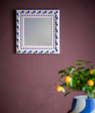 Decorative mirror with floral pattern on a purple wall, next to a plant in a blue pot.