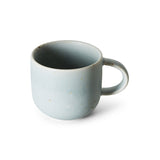 A light blue ceramic mug with a small loop handle and subtle speckled brown glaze details, shown on a clean white background.