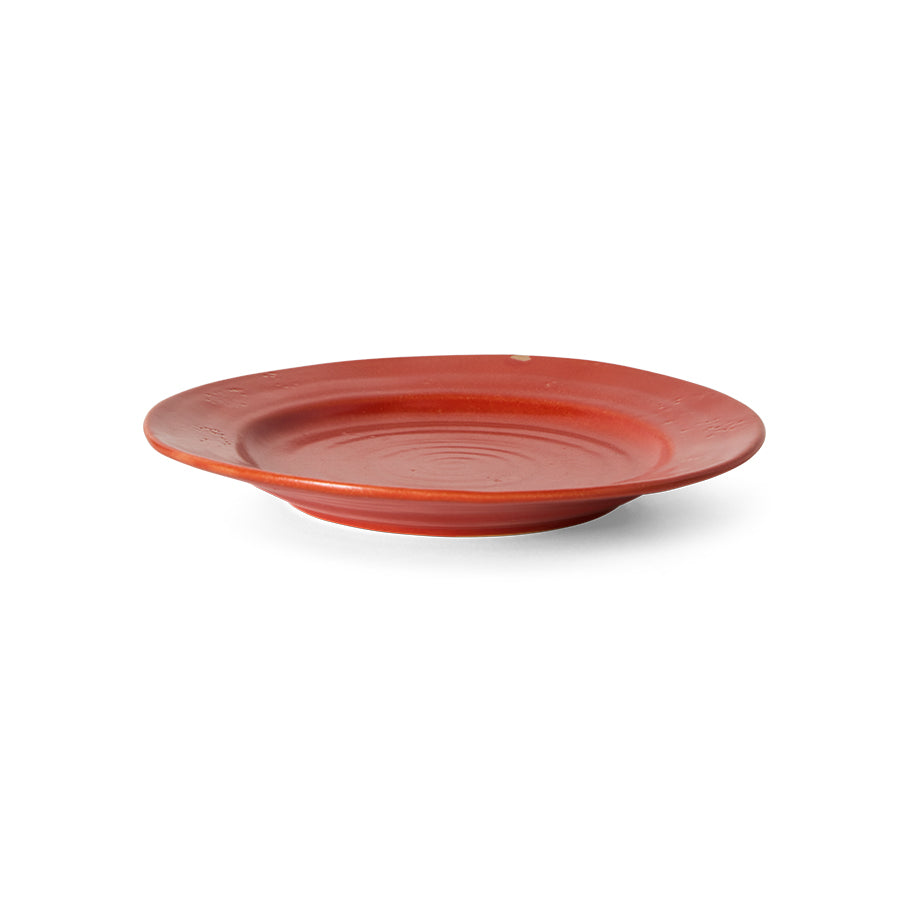 A round terracotta red ceramic plate with a textured, slightly raised rim and concentric ring details in the center, shown on a plain white background.