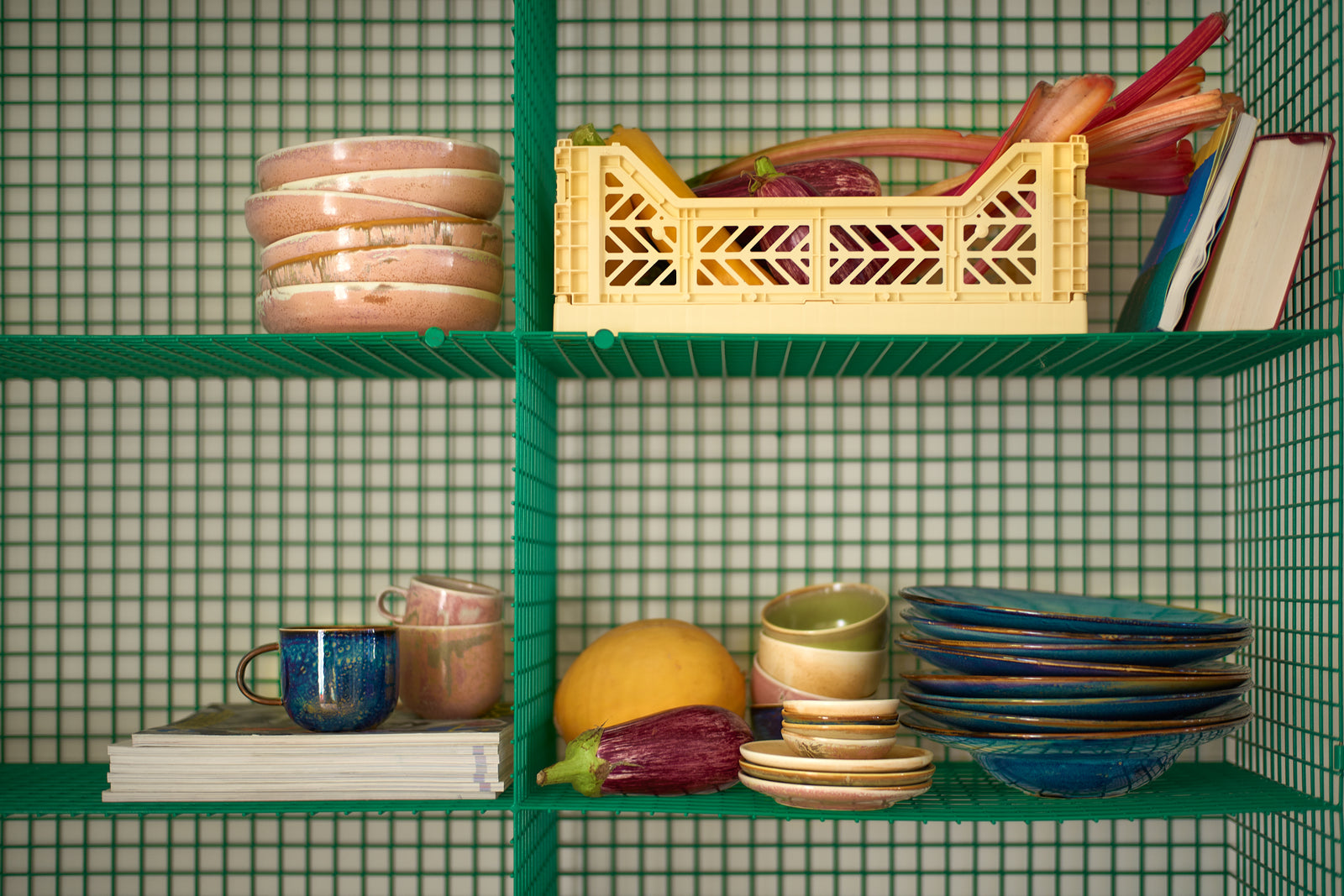Green shelving unit with various items including books, a yellow crate, and ceramic plates against a green tiled wall.