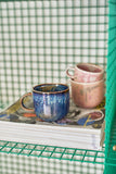 Three ceramic mugs on a stack of books with a green grid background